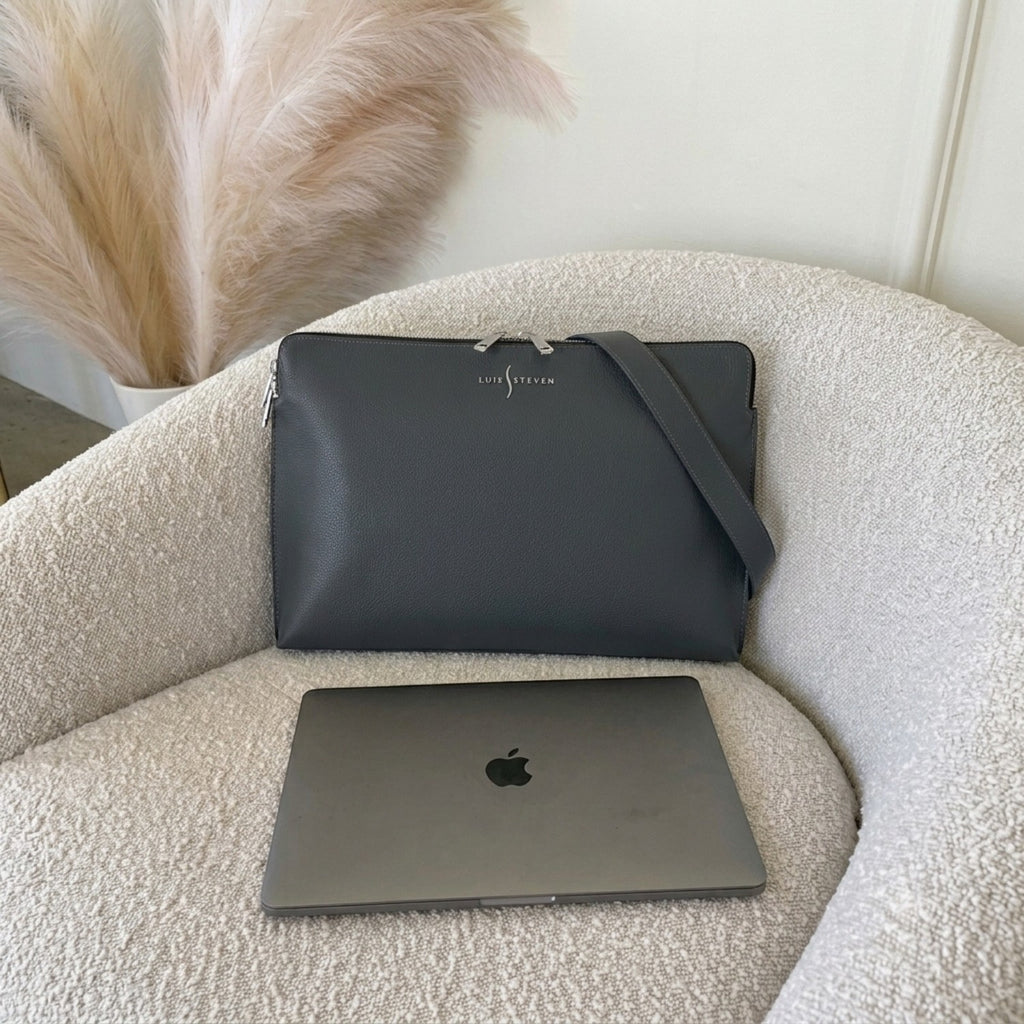 Luis Steven gray pebble leather laptop sleeve with detachable shoulder strap resting on a textured cream chair.
