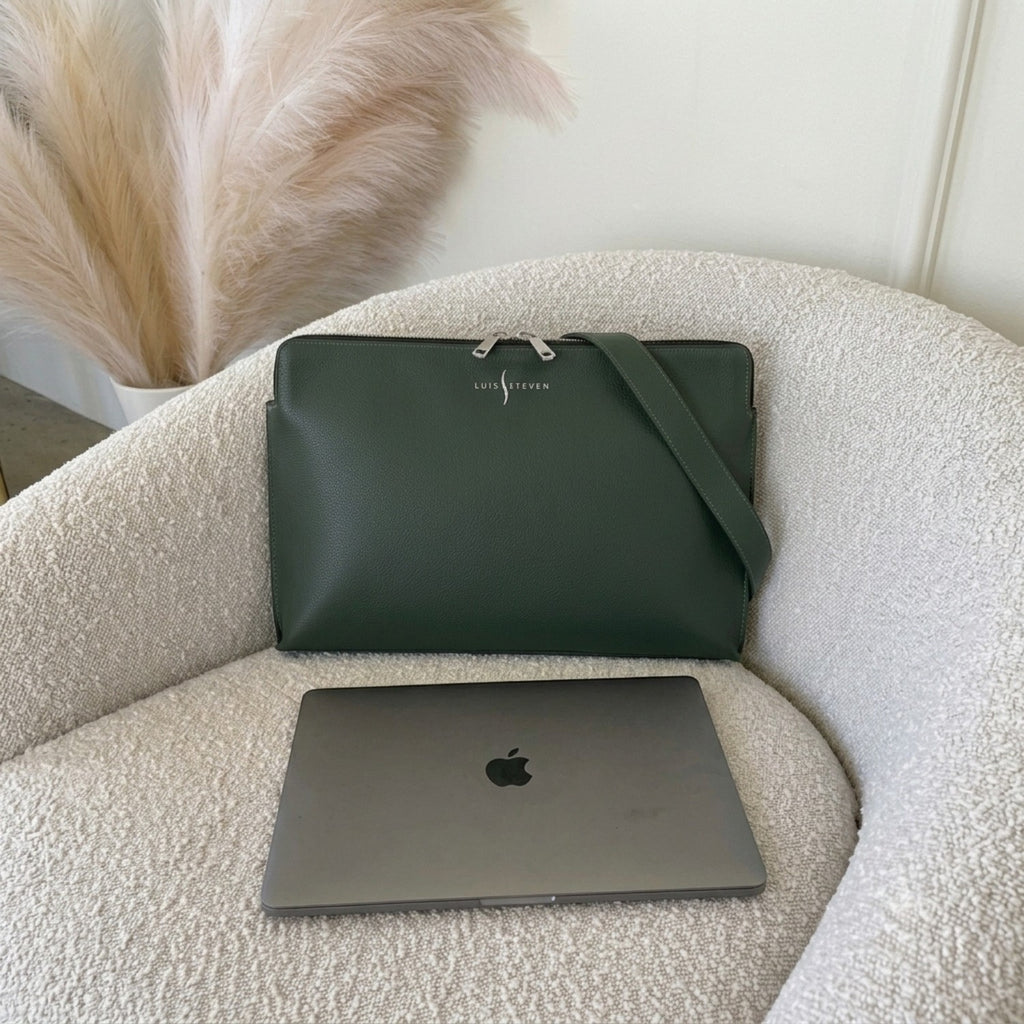 Luis Steven green Italian pebble leather laptop sleeve with detachable shoulder strap resting on a textured chair.