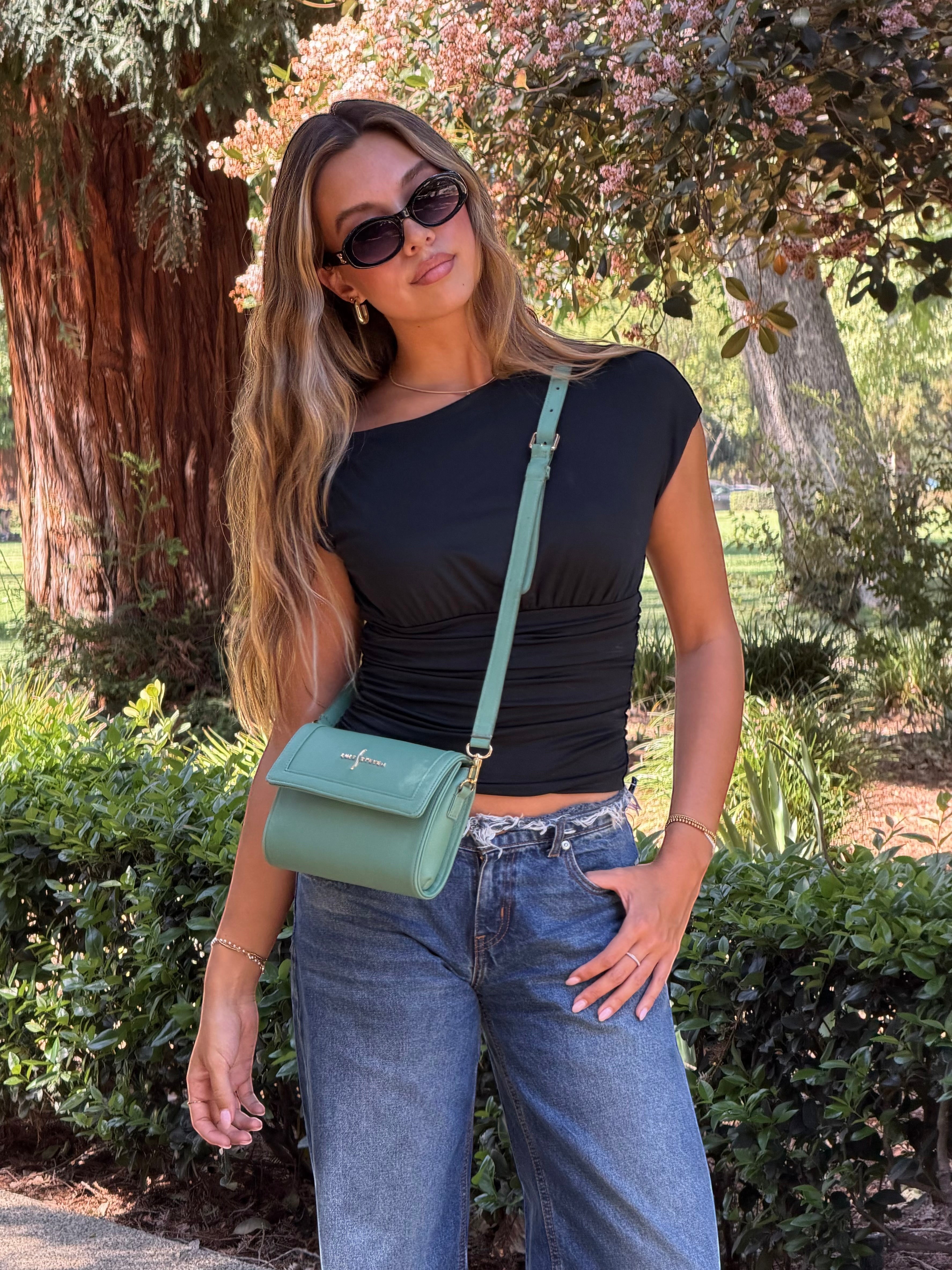 Luis Steven sage green pebble leather crossbody bag with gold hardware and flap closure, worn by a model outdoors.