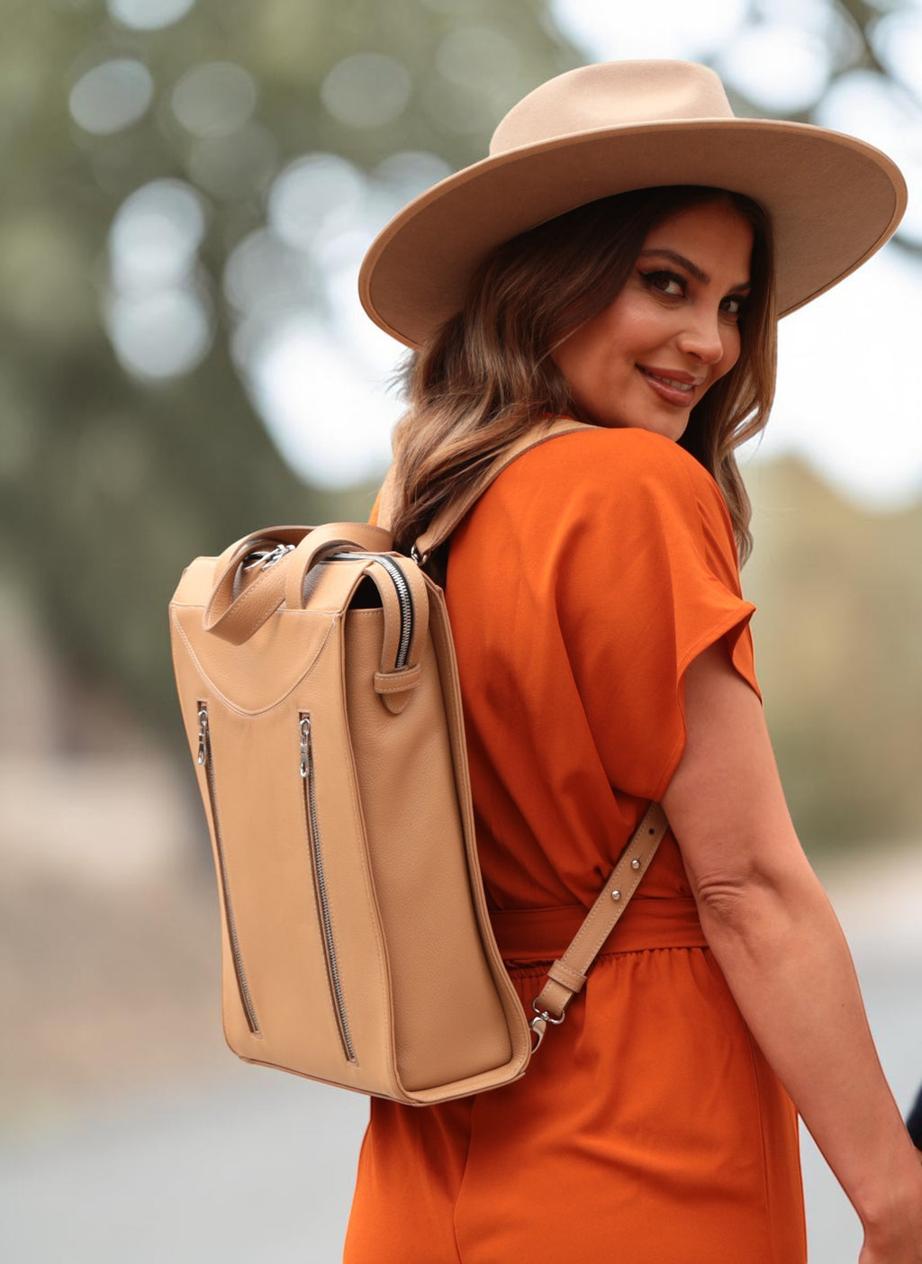 Luis Steven sand pebble Italian leather tote style backpack with removable straps, worn by a woman in an orange jumpsuit and hat.